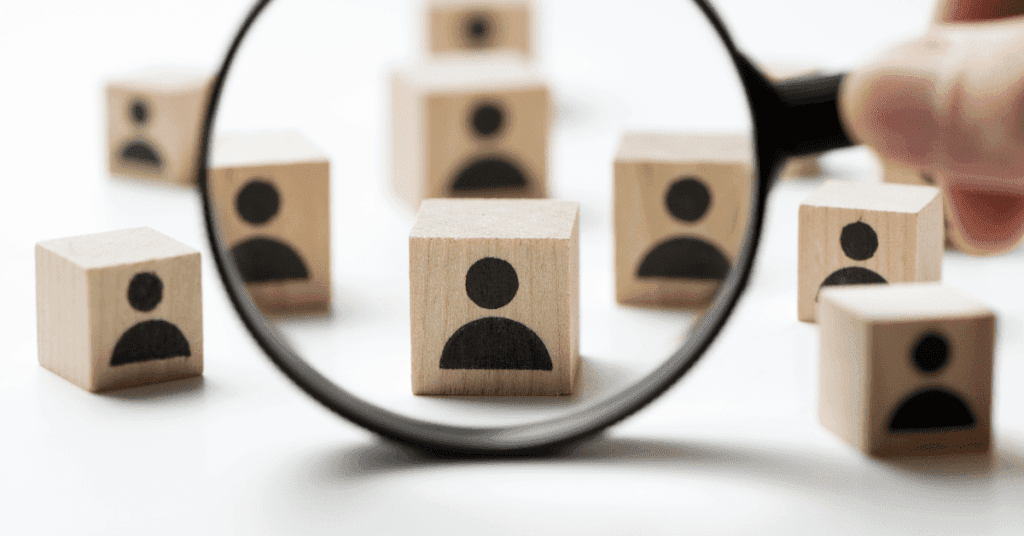 Magnifying glass focused on a wooden block with a user icon, symbolizing talent selection and vendor evaluation in IT outsourcing.