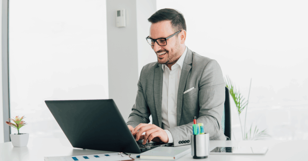 Happy business executive working confidently on a laptop in a bright office, representing satisfaction with a reliable outsourcing solution.
