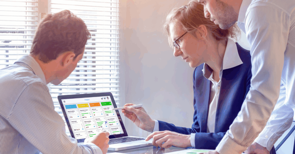 Team discussing a Kanban board on a laptop screen, collaborating to track tasks and manage agile development processes effectively.