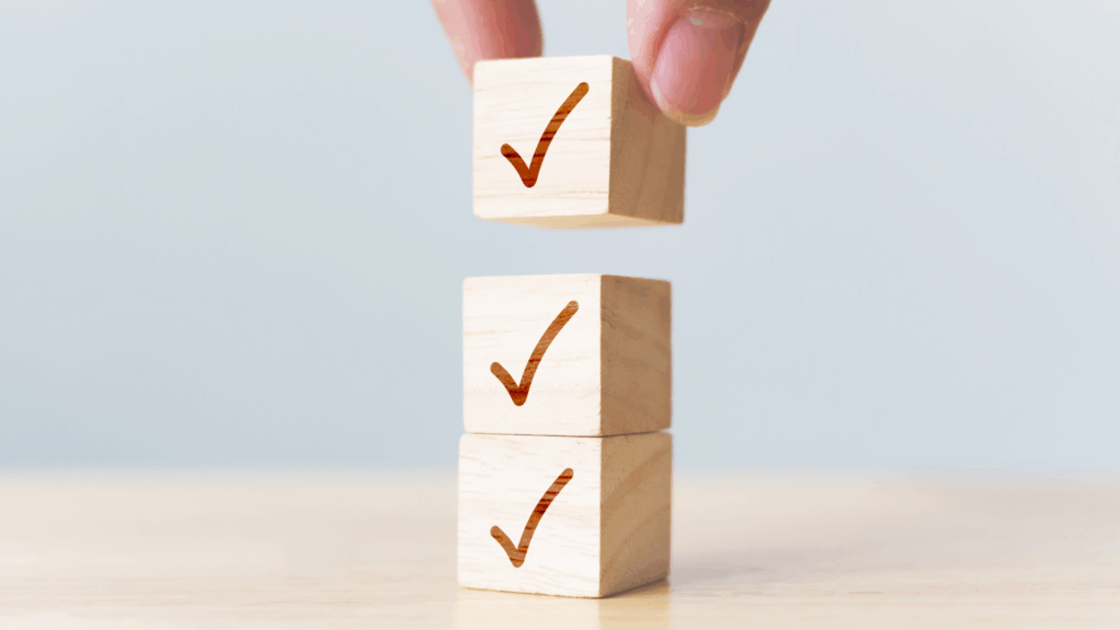 Hand stacking wooden blocks with checkmarks, symbolizing quality control and selection in nearshore staffing services.