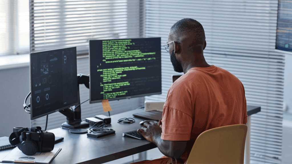 Developer programming with green code displayed across dual monitors in a modern workspace