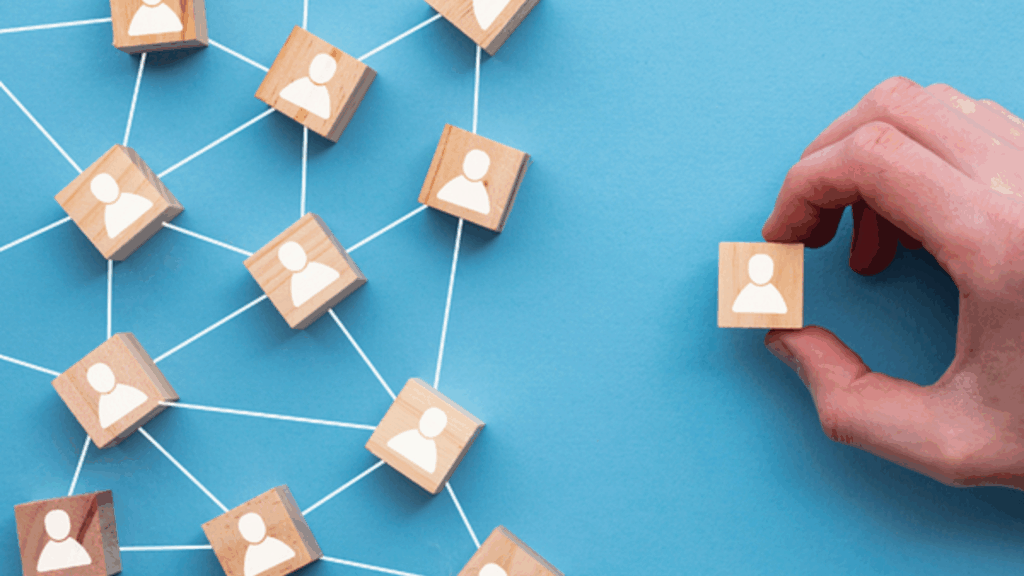 Hand placing a wooden block with a user icon into a connected network of blocks, symbolizing team scalability and staff augmentation strategy.