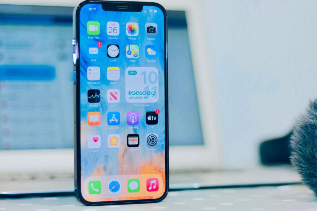 parallelstaff- A smartphone with a colorful home screen displaying various app icons stands upright on a table, suggesting the need to hire an Android app developer, with a blurred laptop and other objects in the background.