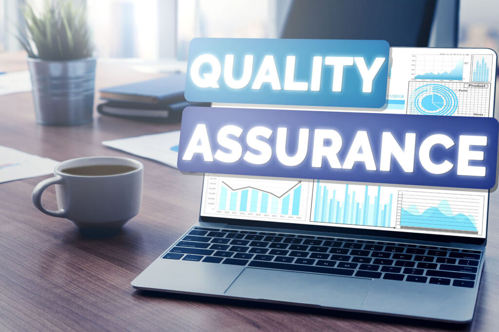 parallelstaff- A laptop displaying data charts sits on a desk next to a coffee cup and plant. The words Quality Assurance are prominently overlaid, highlighting the focus on what does a QA engineer do in ensuring software reliability and performance.