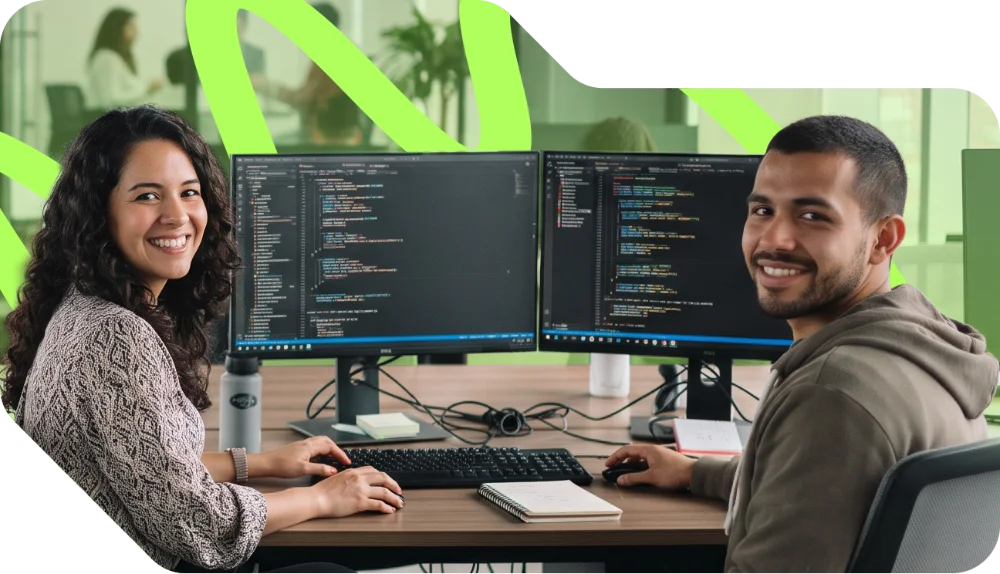 parallelstaff- Two people sit at a desk with dual monitors displaying code, smiling at the camera in a modern office setting. A notebook and water bottle are on the desk. Green abstract lines are in the background.
