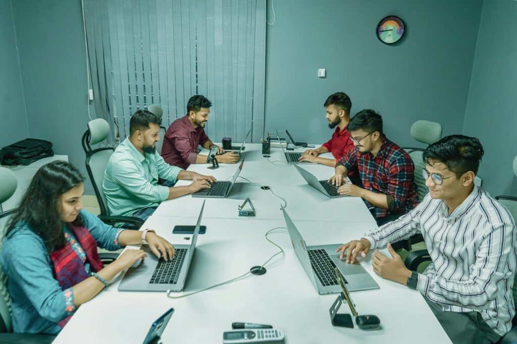 a group of people sitting around a table with laptops